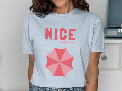 Light blue t-shirt with "NICE CÔTE D'AZUR" and a pink umbrella graphic.
