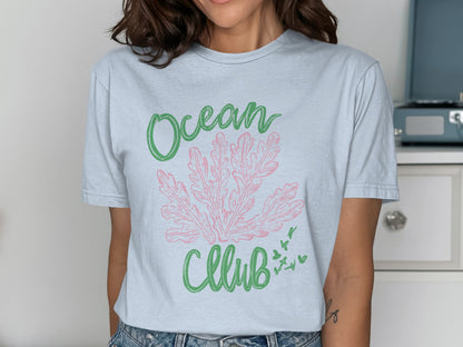 Light blue t-shirt with pink coral and green text "Ocean Club" with small birds.