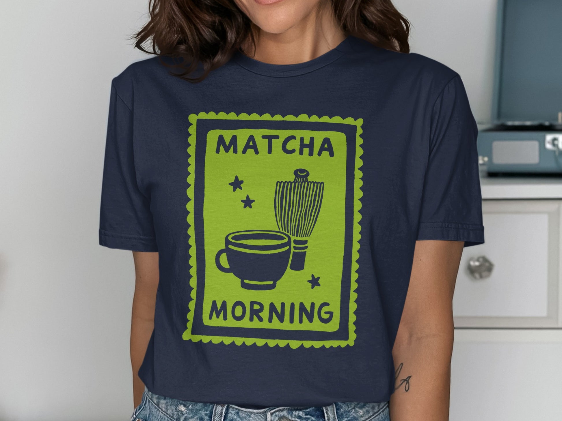 Green graphic with teacup, whisk, and "Matcha Morning" text on navy t-shirt.