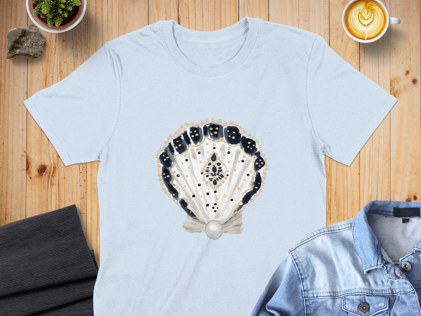 Light blue t-shirt with a watercolor shell design featuring black dots and a pearl.