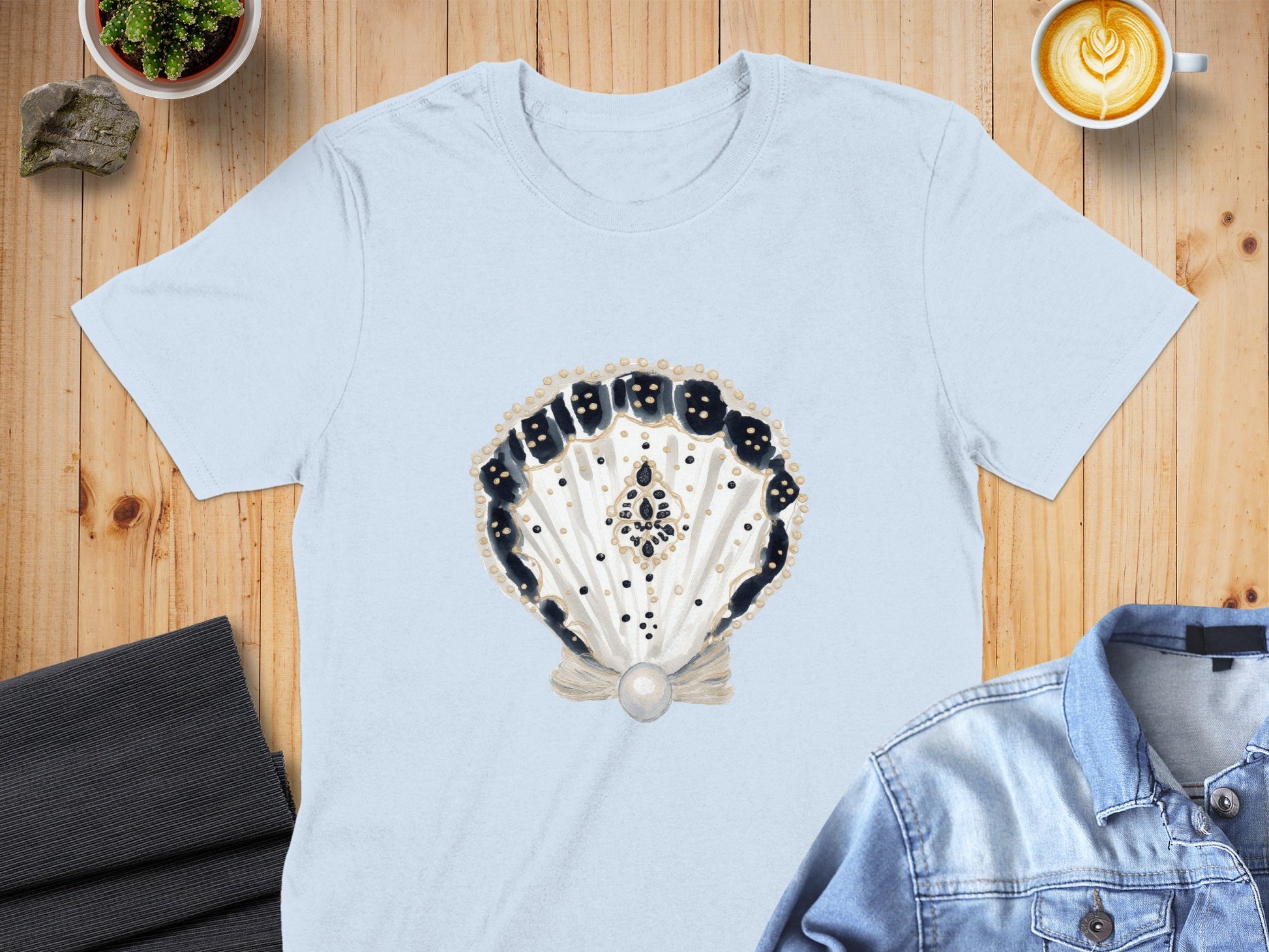 Light blue t-shirt with a watercolor shell design featuring black dots and a pearl.