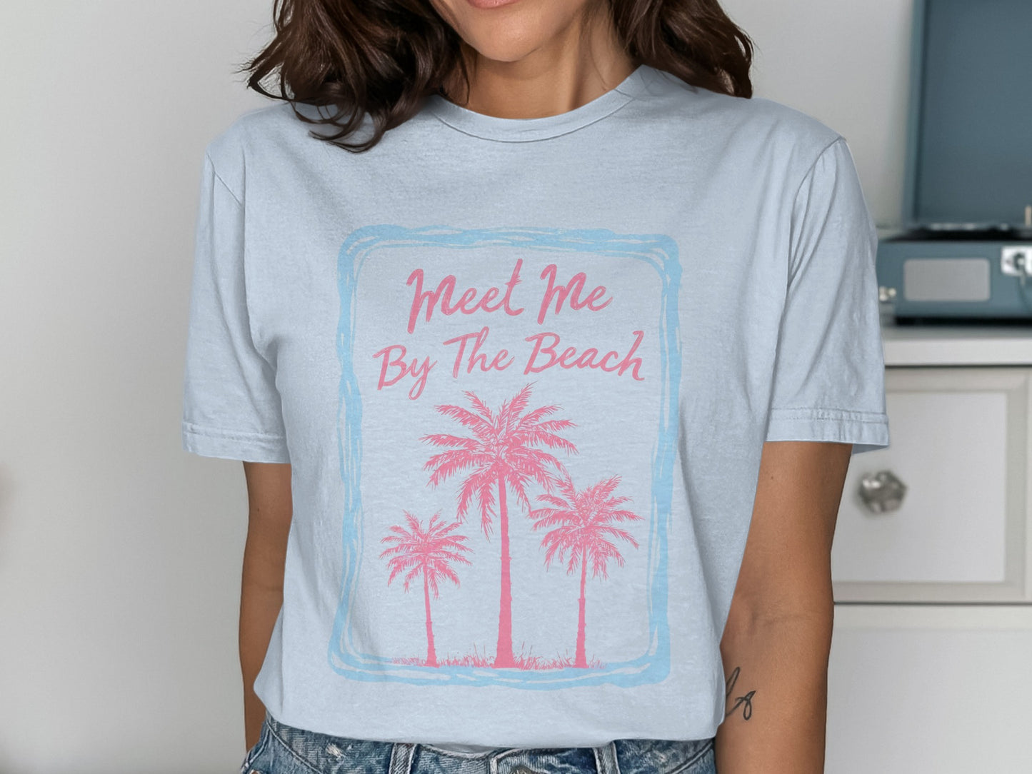 Light blue t-shirt with pink palm trees and "Meet Me By The Beach" text.